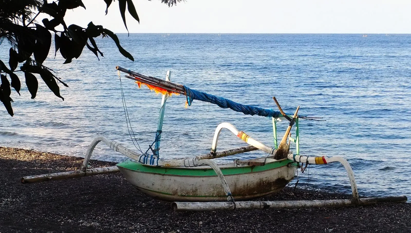 A wooden jukung pulled up on a dark pebble beach